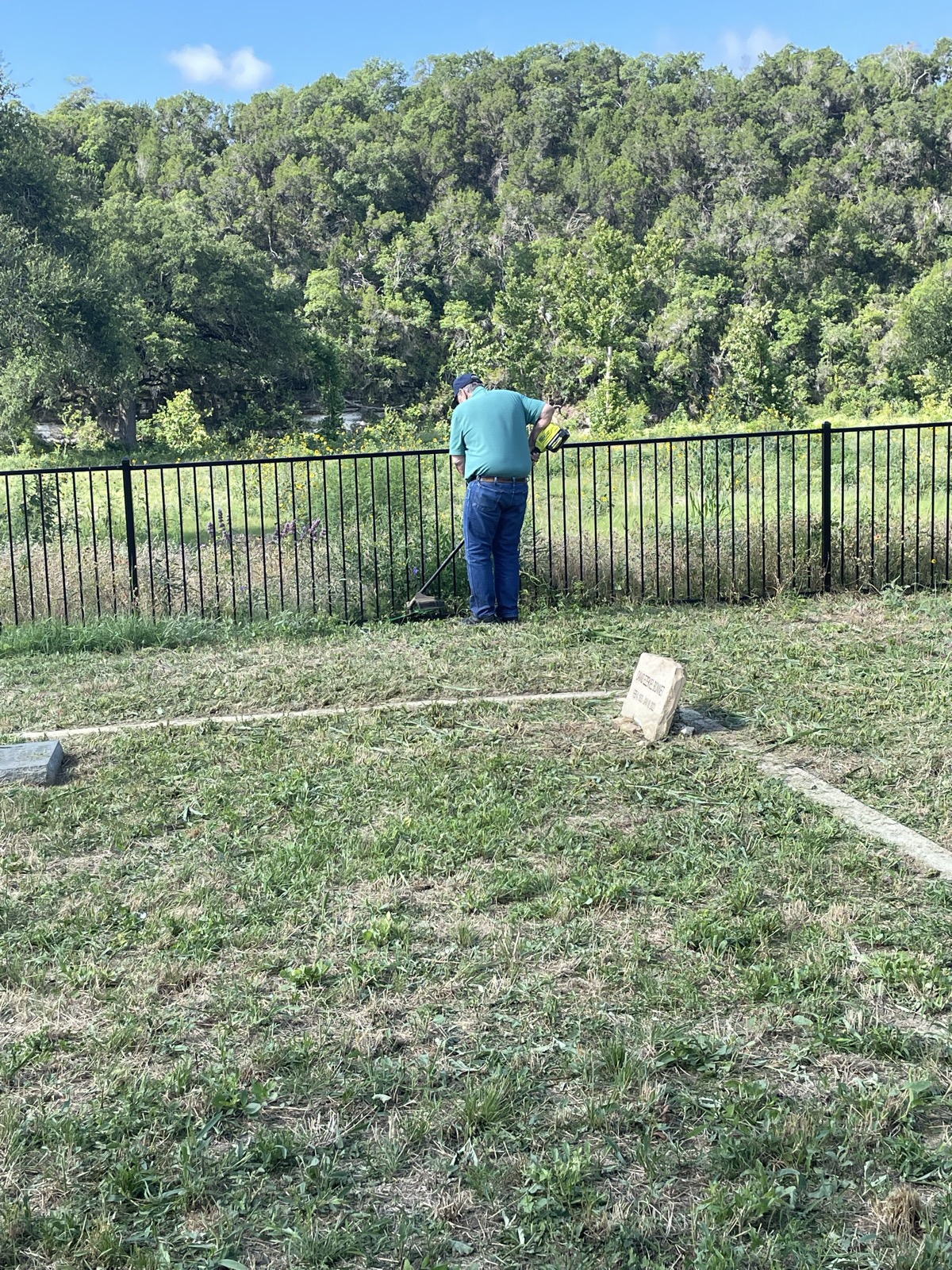 A volunteer clears tall grass and weeds along the cemetery's iron fence.