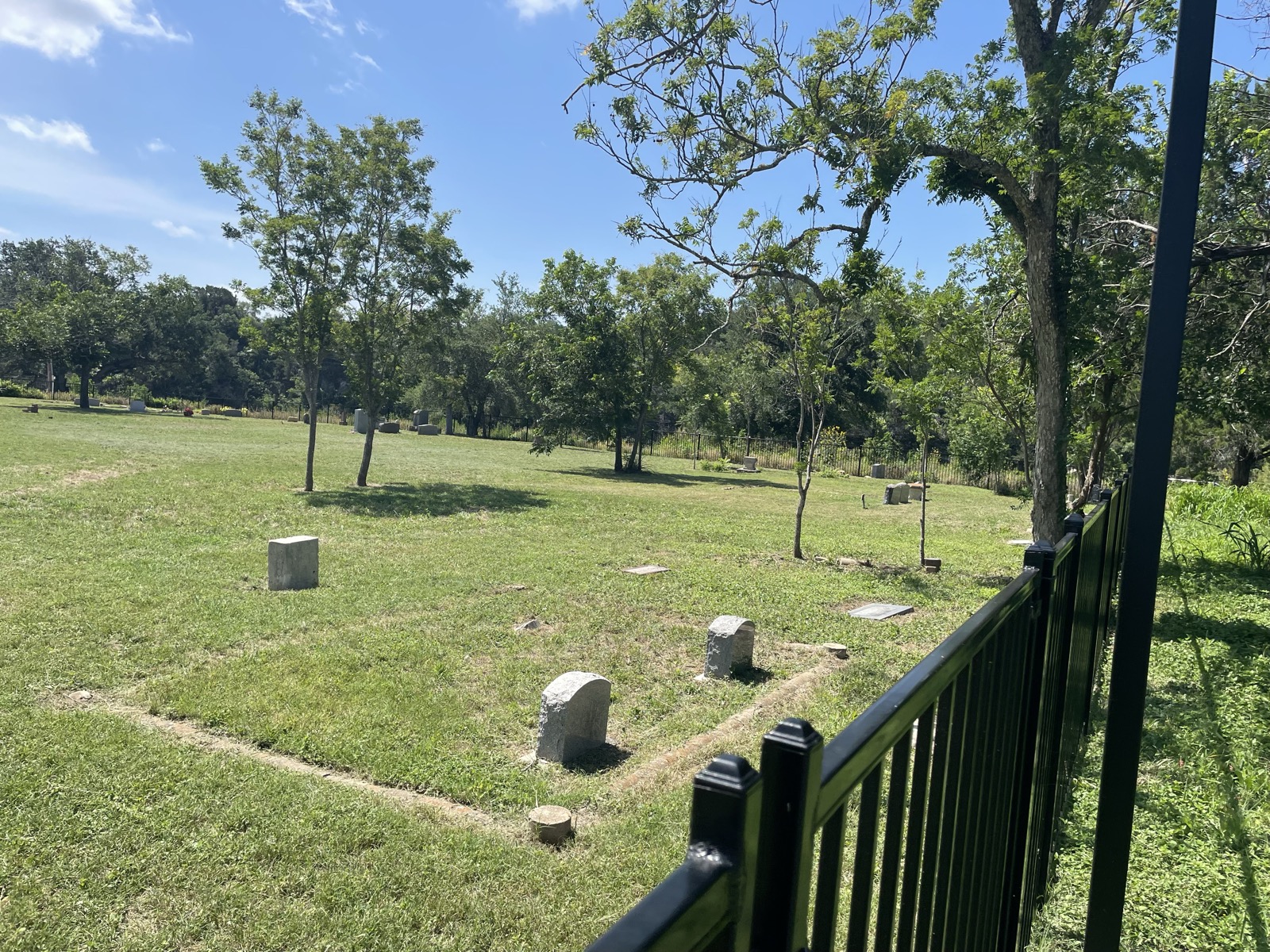 The mowed cemetery grounds with scattered headstones and young trees under a clear sky.