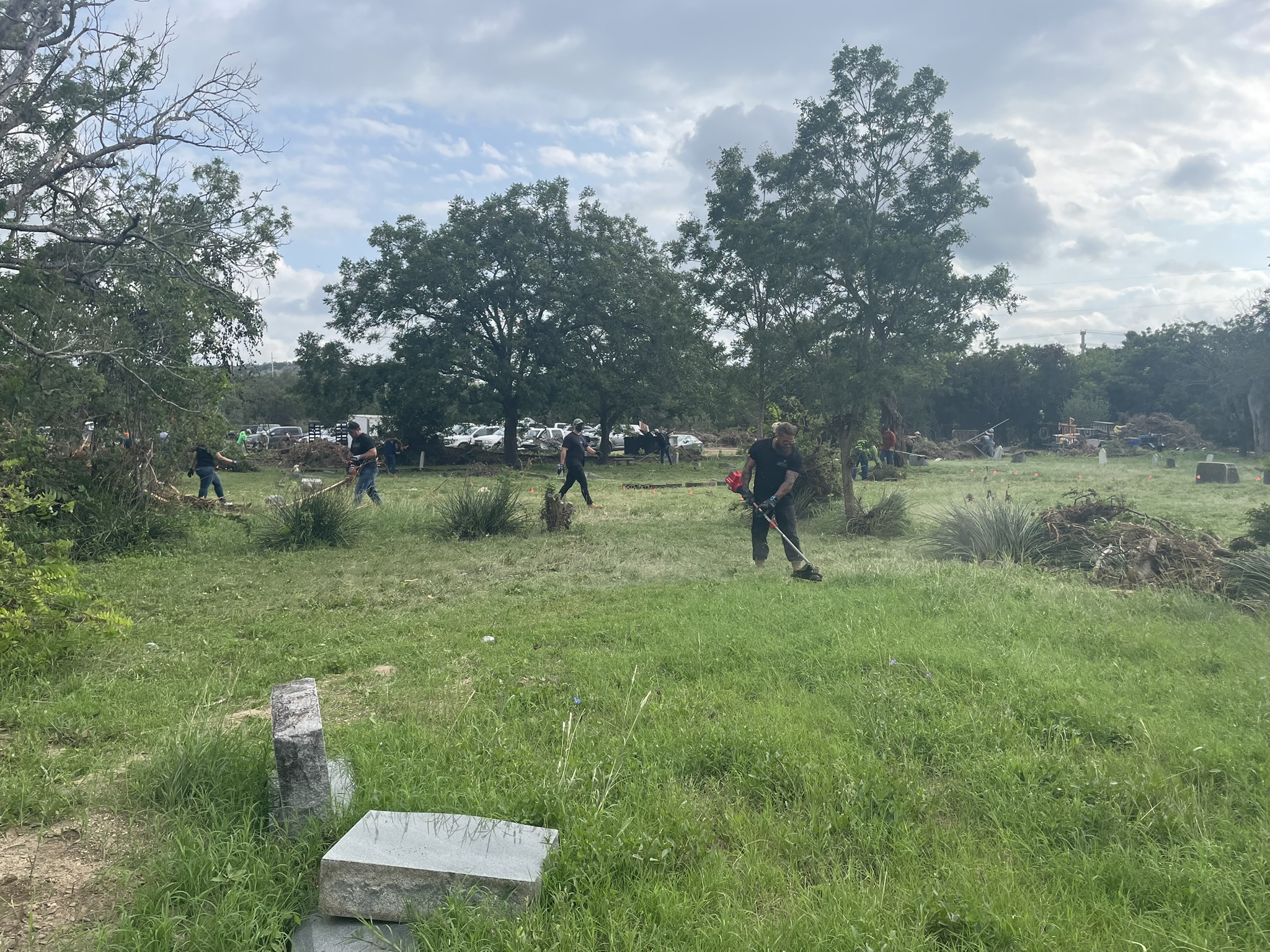 Cleanup crew working with weed eaters and tools across the cemetery